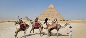 een groep mensen die op kamelen rijden voor de piramiden bij Pyramids Temple Guest House in Caïro