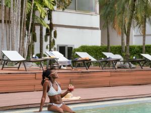 a girl in a bathing suit sitting in a pool with a drink at Novotel Abidjan in Abidjan