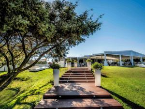 a wooden walkway leading to a building with a tree at Almar Timi Ama Resort & Spa in Villasimius