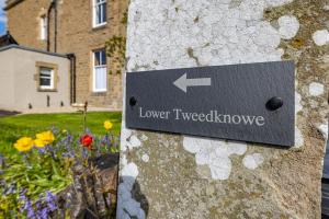 una señal en el costado de una pared de piedra con flores en Lower Tweedknowe - ground floor villa Melrose en Melrose