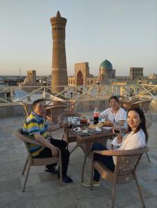 un groupe de personnes assises à une table avec de la nourriture dans l'établissement Hotel POYI KALON terrace حلال, à Boukhara