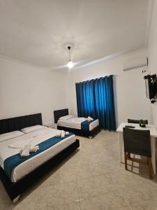 two beds in a room with blue curtains and a table at DEA Room 2 in Sarandë