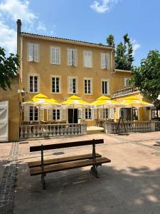 a bench in front of a building with yellow umbrellas at Hôtel de la Loube in La Roquebrussanne +20 photos
