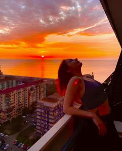a woman looking out of a window at the sunset at Orbi City apartment with sea view in Batumi