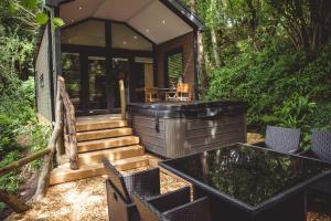 Caerwys的住宿－Herons Lake Retreat Lodges，一座小房子,在树林里设有一个浸泡浴缸