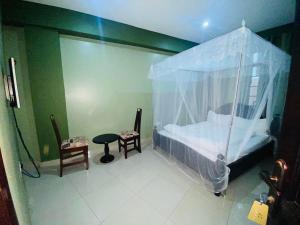 Suzie hotel في كامبالا: غرفة نوم بسرير مظلة وطاولة وكرسي