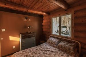 Dormitorio con cama y ventana en una cabaña de madera en Le Petit Domaine Caché - Lac-Simon, en Lac-Simon