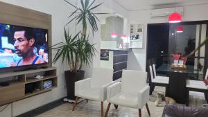 uma sala de estar com cadeiras brancas e uma televisão de ecrã plano em Apartamento no Guarujá - Enseada no Guarujá