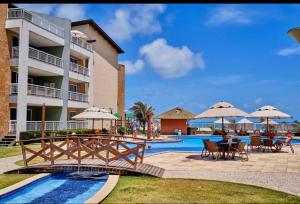 a resort with a pool and tables and chairs and umbrellas at Apartamento Vista total do Mar uma cobertura a 400m do Beach Park no Porto das Dunas Aquiraz Condomínio Terramaris Piscina ampla Parque infantil Sauna Estacionamento privado in Aquiraz