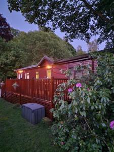 a red cabin with a fence and pink flowers at Windermere lodge,sleeps 6 in Windermere