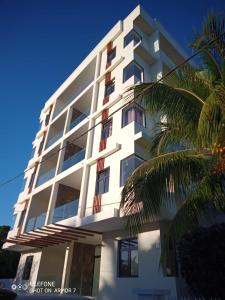 a white building with a palm tree in front of it at Kensington square in Flic-en-Flac