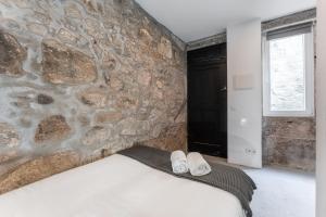 a bedroom with a stone wall and two white slippers at Sao Victor Suites in Porto