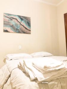 uma cama com lençóis brancos e uma pintura na parede em Energia Perfeita Casa Solar Milagres em Americana
