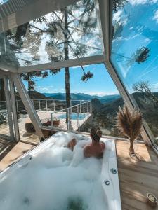 a man in a bath tub with a view of the mountains at Chalé Aframe- Benta Rosa Chalés de Luxo in Urubici