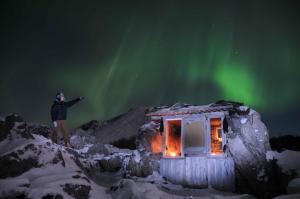 une personne debout à côté d'une cabine sous les feux du nord dans l'établissement Borghildstua Feriehus, à Melbu