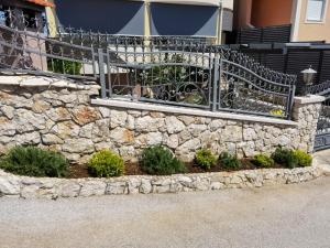 a stone retaining wall with a fence and plants at Apartments Annie in Rogoznica
