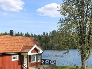 uma casa vermelha com uma árvore ao lado de um lago em Holiday home STENSJÖN em Boda