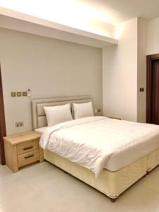 1 dormitorio con 1 cama blanca grande y mesita de noche de madera en Iveria Hotel Apartments en Ḩayl Āl ‘Umayr