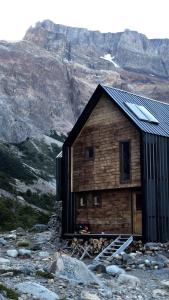 una cabaña de madera en una montaña con montañas en el fondo en Puesto Cagliero - Refugio de montaña en El Chaltén