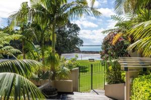a view of a garden with palm trees and the ocean at Beachside Bliss Castor Bay - Holiday by the Beach in Auckland