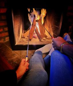 two people sitting in front of a fireplace with their feet on a stick at Pousada Capanna del Vale - Vale dos Vinhedos in Bento Gonçalves
