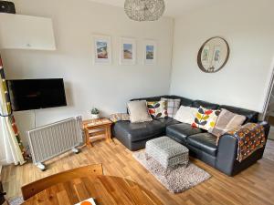 a living room with a black leather couch and a tv at Barn Owls Holiday Bungalow in Salcombe Regis
