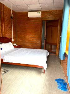 1 dormitorio con cama blanca y pared de ladrillo en Du Nam Riverside Tour Trọn Gói, en Tân Phú