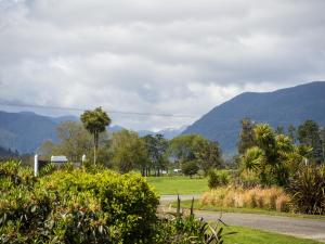 a road in a field with mountains in the background at Karamea River Motels in Karamea