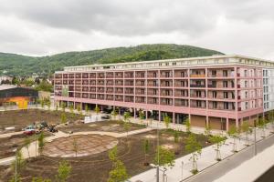 a large pink building with a mountain in the background at Muzeta Graz - Eco-Friendly Parkview Holiday Apartments in Graz’s Smart City in Graz