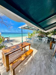 un banco de madera sentado en la playa bajo una sombrilla en Bougainvillea Inn - Maldives, en Fulidhoo