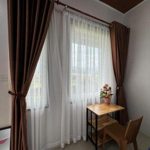 uma janela com cortinas e uma mesa com um vaso de flores em Sapo Rumbia Villa & Hotel em Berastagi