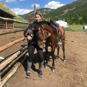 een vrouw die naast een bruin paard staat bij Dream Adventure Mongolia in Nalayh