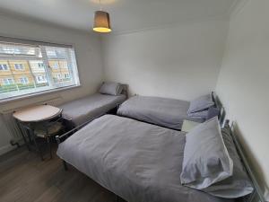 a bedroom with two beds and a table and a window at GATWICK ROOMs in Ifield