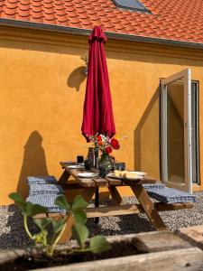 a picnic table with a red umbrella next to a building at Ellens Have, Lejlighed Asta in Ebeltoft