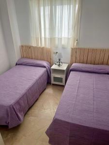 2 Betten in einem Schlafzimmer mit violetter Bettwäsche und einem Tisch in der Unterkunft Apartamento Pinares del Portil junto a la playa in El Portil