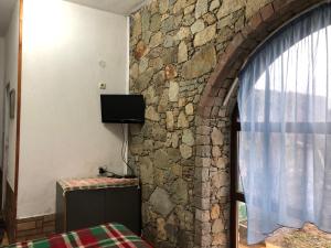 Habitación con pared de piedra y ventana con TV. en Лилянината къща en Kalofer