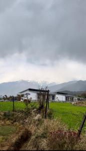 a white barn in a field with mountains in the background at Bir Valley Retreat in Bīr