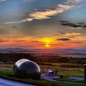 ein Observatorium mit Stühlen und Sonnenuntergang im Hintergrund in der Unterkunft Forth Mountain Glamping in Ballintlea