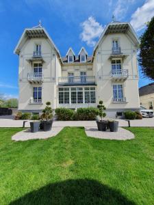 ein großes weißes Haus mit einem grünen Hof in der Unterkunft La Roseraie in Saint-Étienne-au-Mont