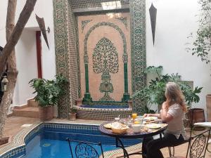una mujer sentada en una mesa frente a una piscina en Riad Alma Mouassine en Marrakech