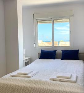 a white bedroom with a bed with blue pillows and a window at Casa Lilla - Ideal for couples in Los Alcázares