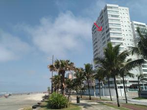 um edifício branco alto com uma bandeira vermelha em cima em Apartamento frente mar pé na areia na Praia Grande