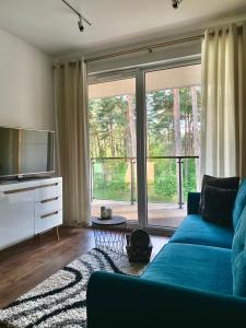 a living room with a blue couch and a large window at REMAR - Apartamentai prie Necko Ežero in Augustów