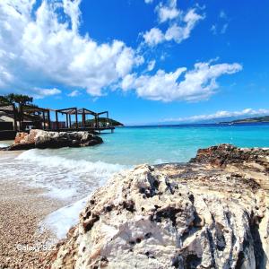 a pier on a beach with blue water and rocks at Residence Vera in Ksamil