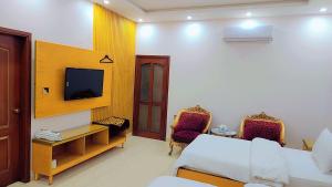 Habitación con cama, TV y sillas. en Clifton Lodge Boutique Hotel en Karachi
