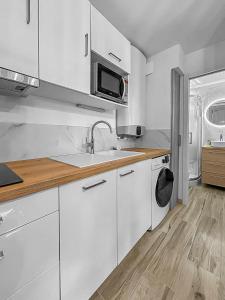 eine Küche mit weißen Schränken, einer Spüle und einer Mikrowelle in der Unterkunft L'évasion paisible à Ouistreham in Ouistreham