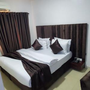 Cama con sábanas blancas y almohadas marrones en Admiralty Hotel, en Lekki