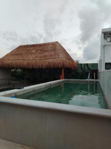 a swimming pool with a thatch roof and a building at Calea Tulum in Tulum