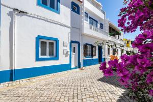 una calle adoquinada con edificios azules y blancos y flores púrpuras en Casa Flores - T2 Santa Luzia - Tavira, en Santa Luzia