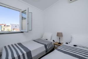 Duas camas num quarto branco com uma janela em Casa Flores - T2 Santa Luzia - Tavira em Santa Luzia